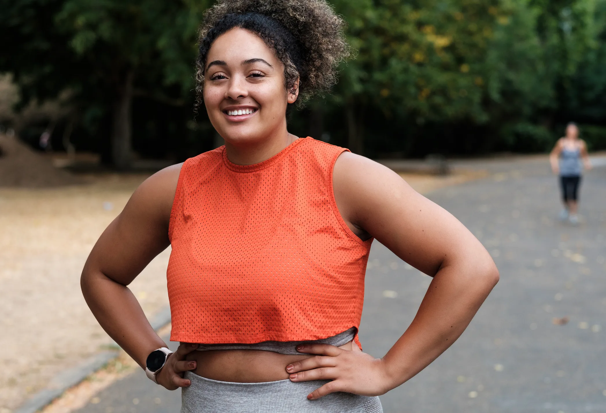 Smiling, active woman standing confidently on a park path after a workout